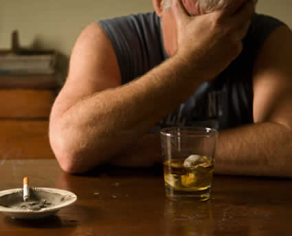 man with head in his hand with glass of liquor in front of him