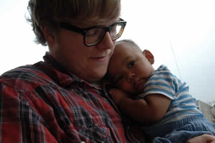 Young man in a plaid shirt dearly holding a young boy