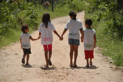 four children walking down dirt path holding hands
