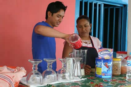 Young man in a blue shirt with a young lady making fruit shakes and juices