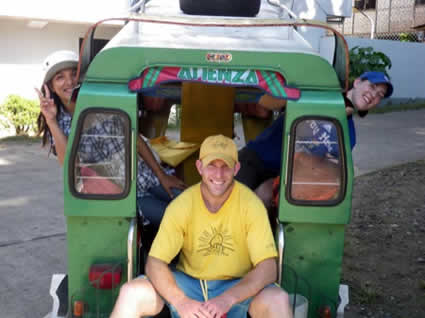 man sitting on back of vehicle and two women sticking heads out of side of vehicle