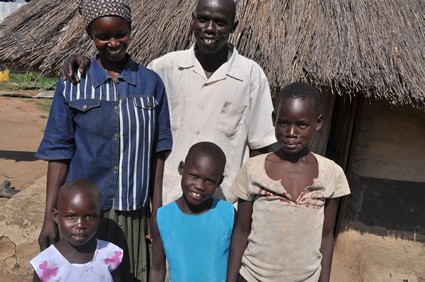 Man woman and three children standing outside a grass hut.