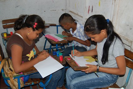 three students sitting at desks painting