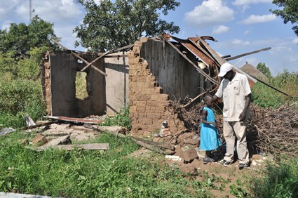 Man and small child standing outside a destroyed house.