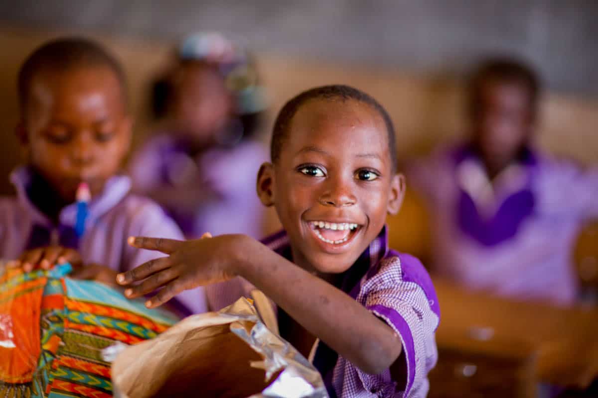 What Does the Bible Say About Giving? A boy in a purple school uniform opens a brightly wrapped present.