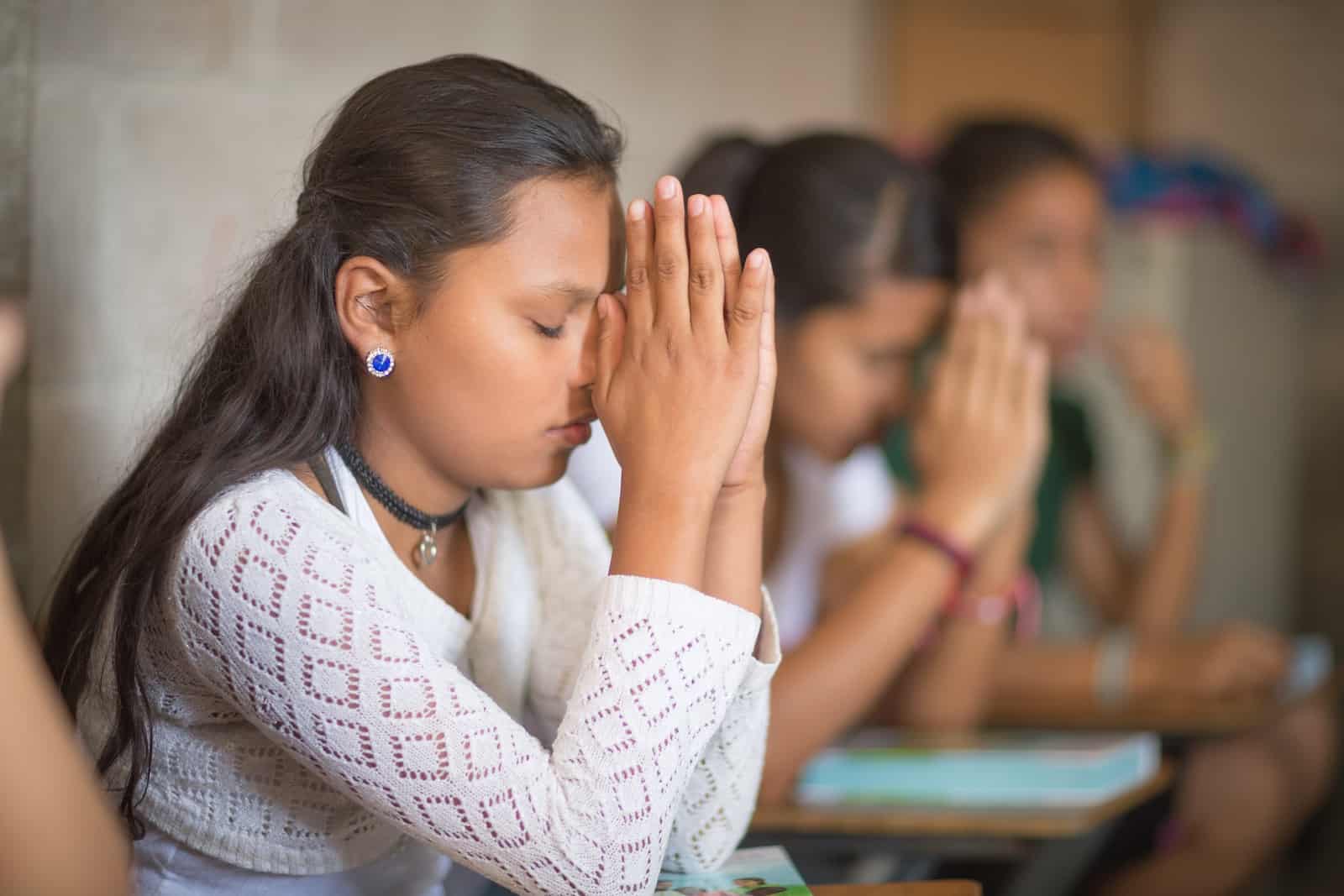 Brokenness Before God - a teenage girl sits at a desk, praying, with her hands held up to her face.