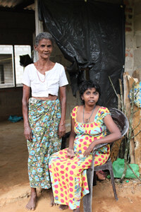 An elderly woman stands next to a woman sitting in a chair