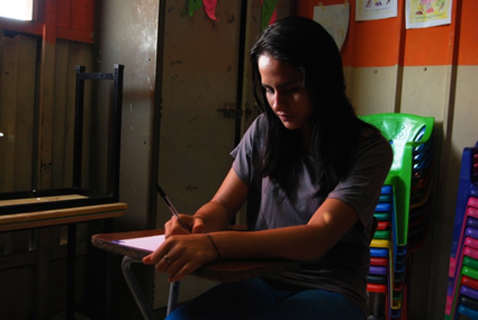 a woman sitting in a green chair writing on a piece of paper