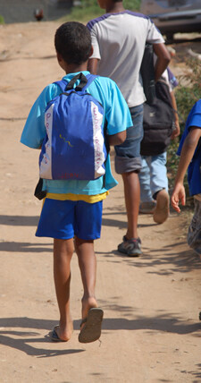 children walking along dirt road with one boy wearing a backpack