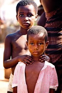 child in red shirt with another child standing behind them with hands on shoulders
