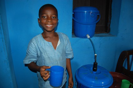 smiling boy holding a cup in front of water filtration system