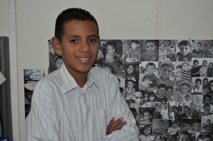 smiling young boy with photos of children behind him