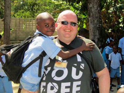 Man with sunglasses holding on to a child in a blue shirt with a black backpack