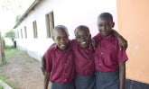 Three smiling children wearing burgandy shirts and gray skirts