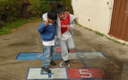 boy assisting another boy as they play hopscotch