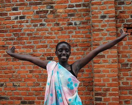 young Rwandan smiling girl standing in front of red brick with hands in the air