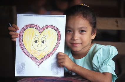 smiling girl in blue dress holding a drawing of a heart