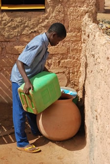 young boy pouring water into large clay pot