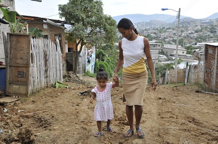 woman walking on dirt road through community holding hand of little girl