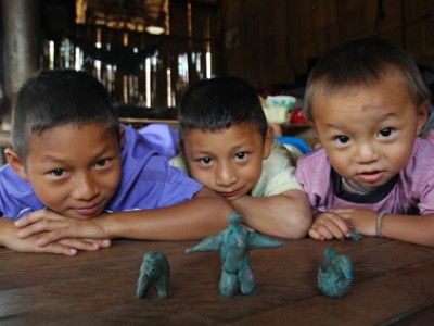 Three boys sitting at a table looking at three green clay figures