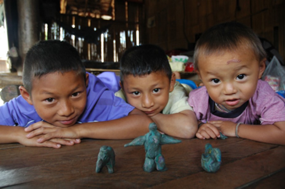 Three boys sitting at a table looking at three green clay figures