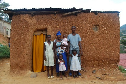 Rwandan family of six standing in front of their earthen home