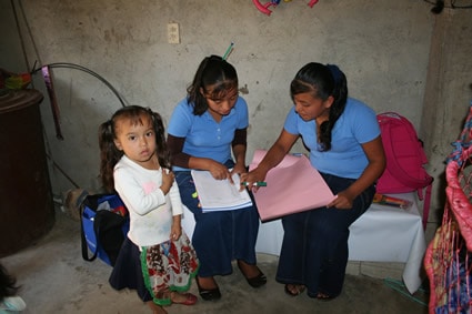 two young women looking at a paper with young girl standing by them