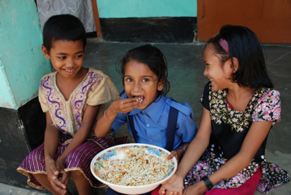 Three children eating rice from a large bowl