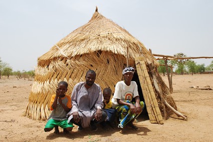 man and woman and two children sitting in front of thatched hut