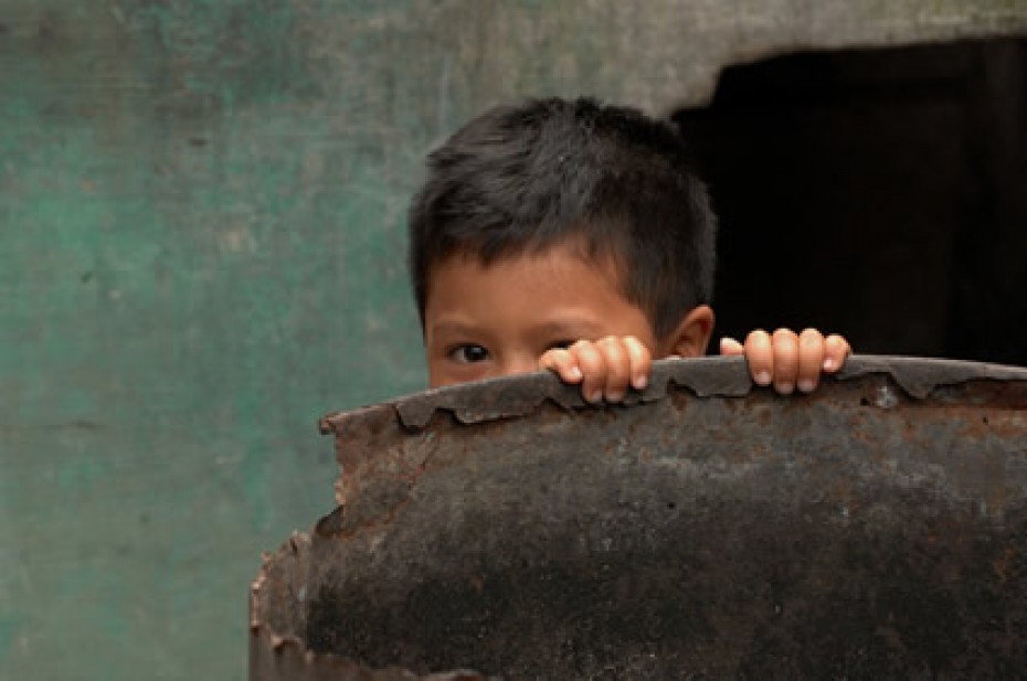 a little boy peeking over the edge of a metal barrel