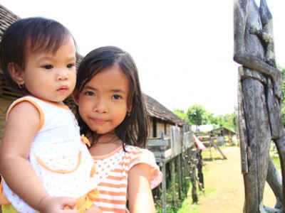 Two young children standing next to a wooden hut.