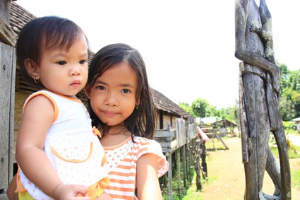 young girl holding a baby girl near a wooden statue