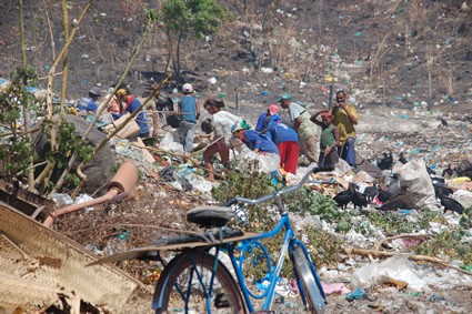 people digging through a dump, blue bicycle in the foreground