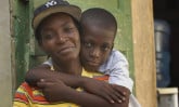 a boy with his arms wrapped around his mother who is wearing a black baseball cap