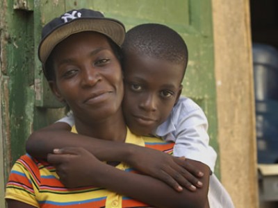 a boy with his arms wrapped around his mother who is wearing a black baseball cap