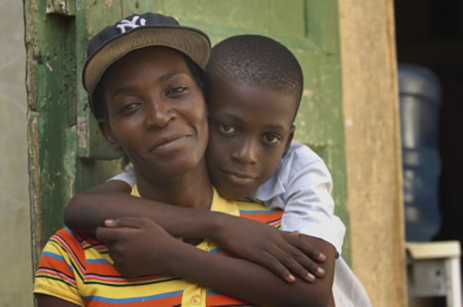 a boy with his arms wrapped around his mother who is wearing a black baseball cap