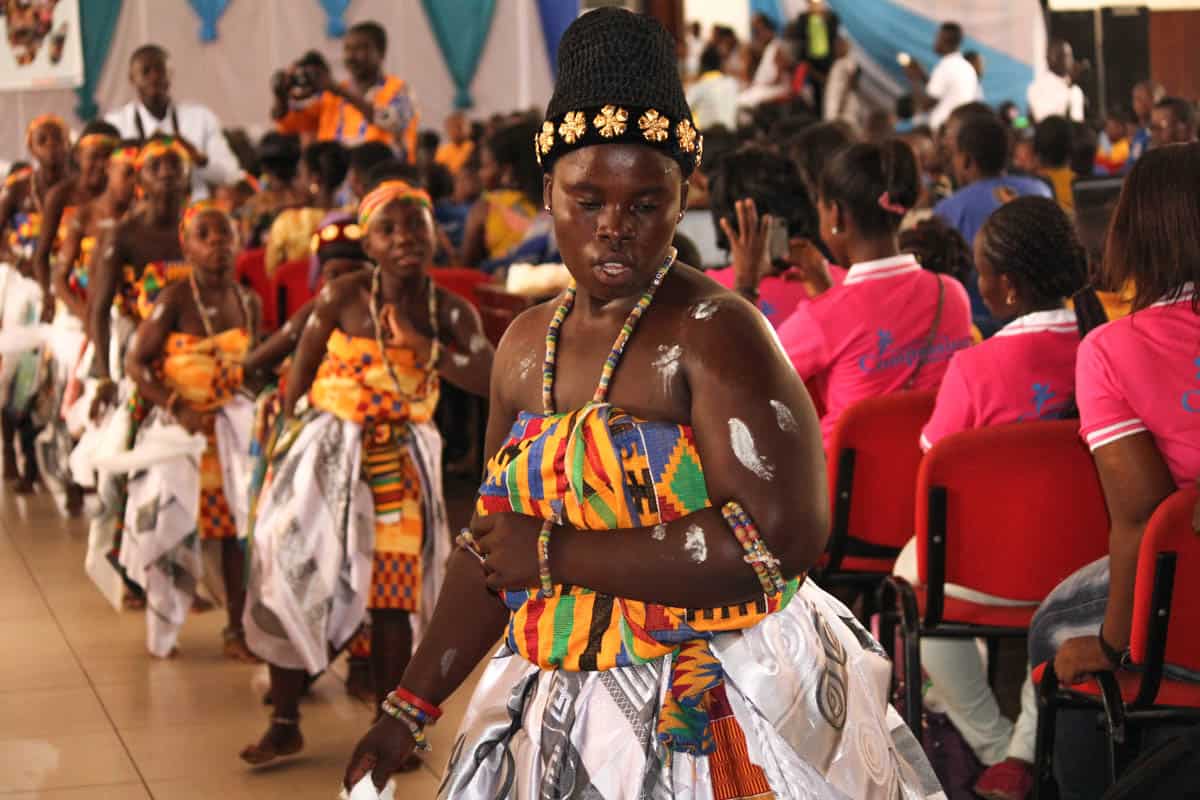 A Ghanaian child smiles while gazing into the distance. The child is wearing traditional Ghanaian clothing for a festive activity.