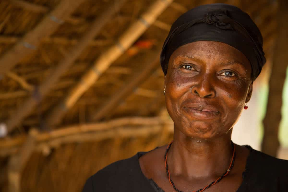 A woman in Ghana smiling. She is wearing a black head wrap.