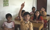 Children in a classroom with one eager boy raising his had to answer the teacher