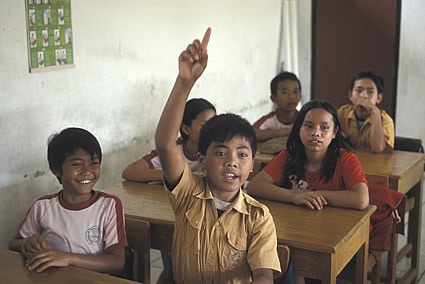children sitting at desks with boy raising hand to answer a question
