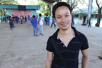 smiling young man in black shirt with children playing in the background