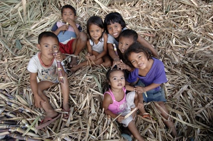 group of boys and girls sitting on a stack of sugar cane husks