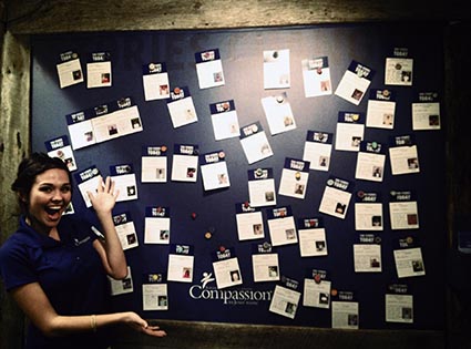 Young lady standing in front of a wall with Compassion childrens' packets