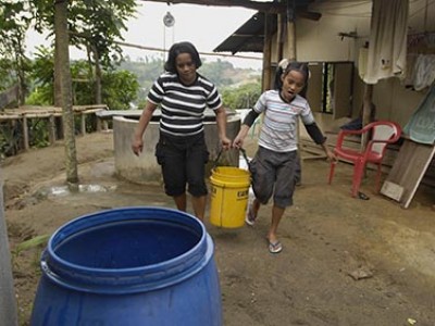 two girls carrying bucket to rain barrel