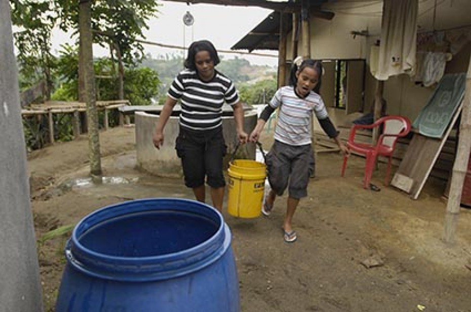 two girls carrying bucket to rain barrel