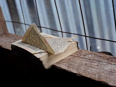 a book with a bent over page sitting on a rough wood shelf