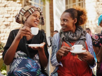 Two women drinking coffee, smiling at each other.