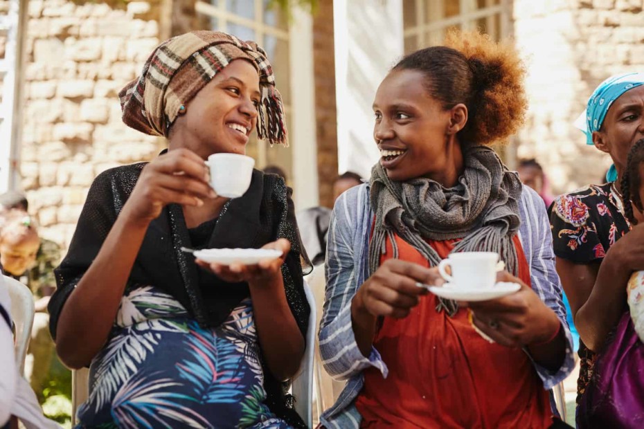 Two women drinking coffee, smiling at each other.