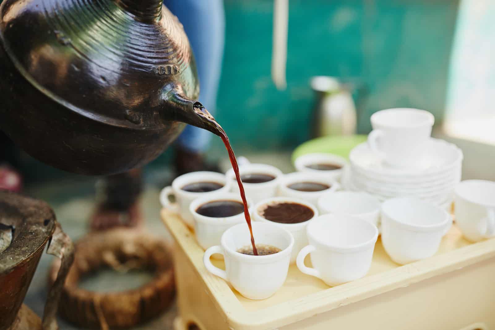 A jebena pours coffee into small cups.
