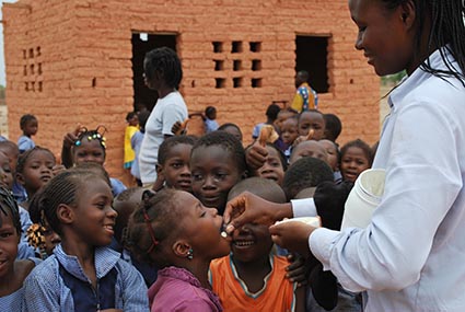 woman wearing a white jacket giving medicine to a group of children